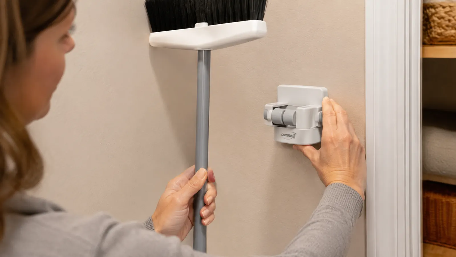 Hand pressing an adhesive broom gripper against the inside wall of a closet before hanging a broom handle in it
