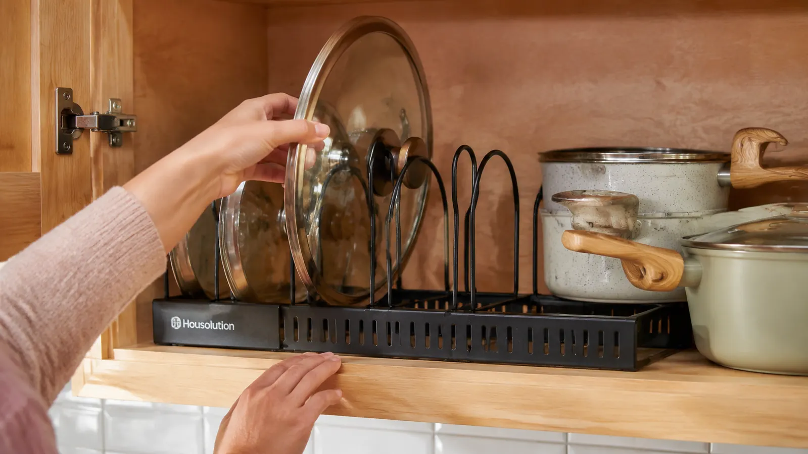 Hand sliding a large Dutch oven lid into an expandable wire pot lid organizer inside a cabinet