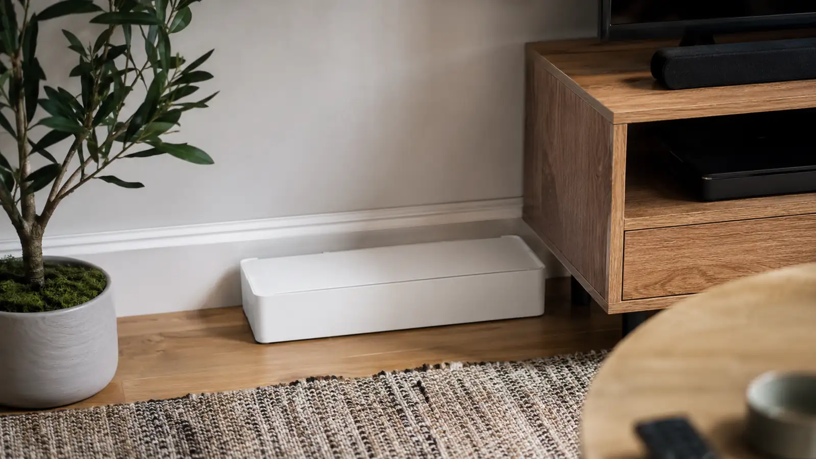 Finished cable management box sitting neatly against the baseboard behind a TV stand with no visible cords