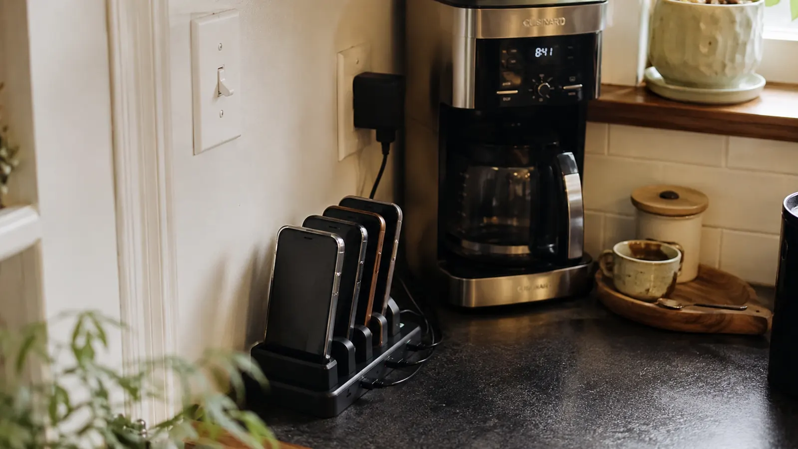 Tidy kitchen counter corner with a charging station holding several phones upright, warm morning light