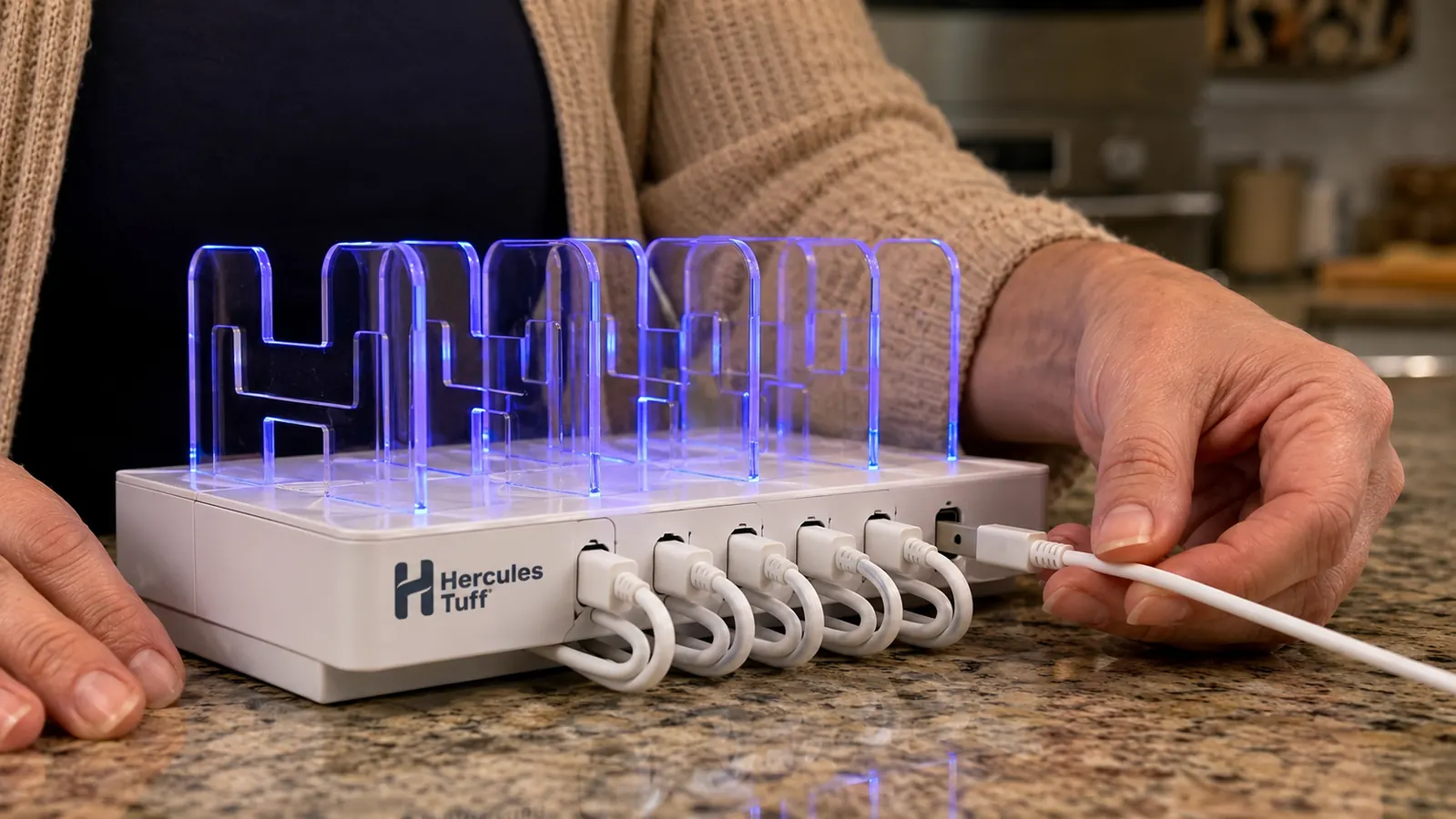 Hand plugging a phone into one of six open ports on a black charging station dock on a kitchen counter