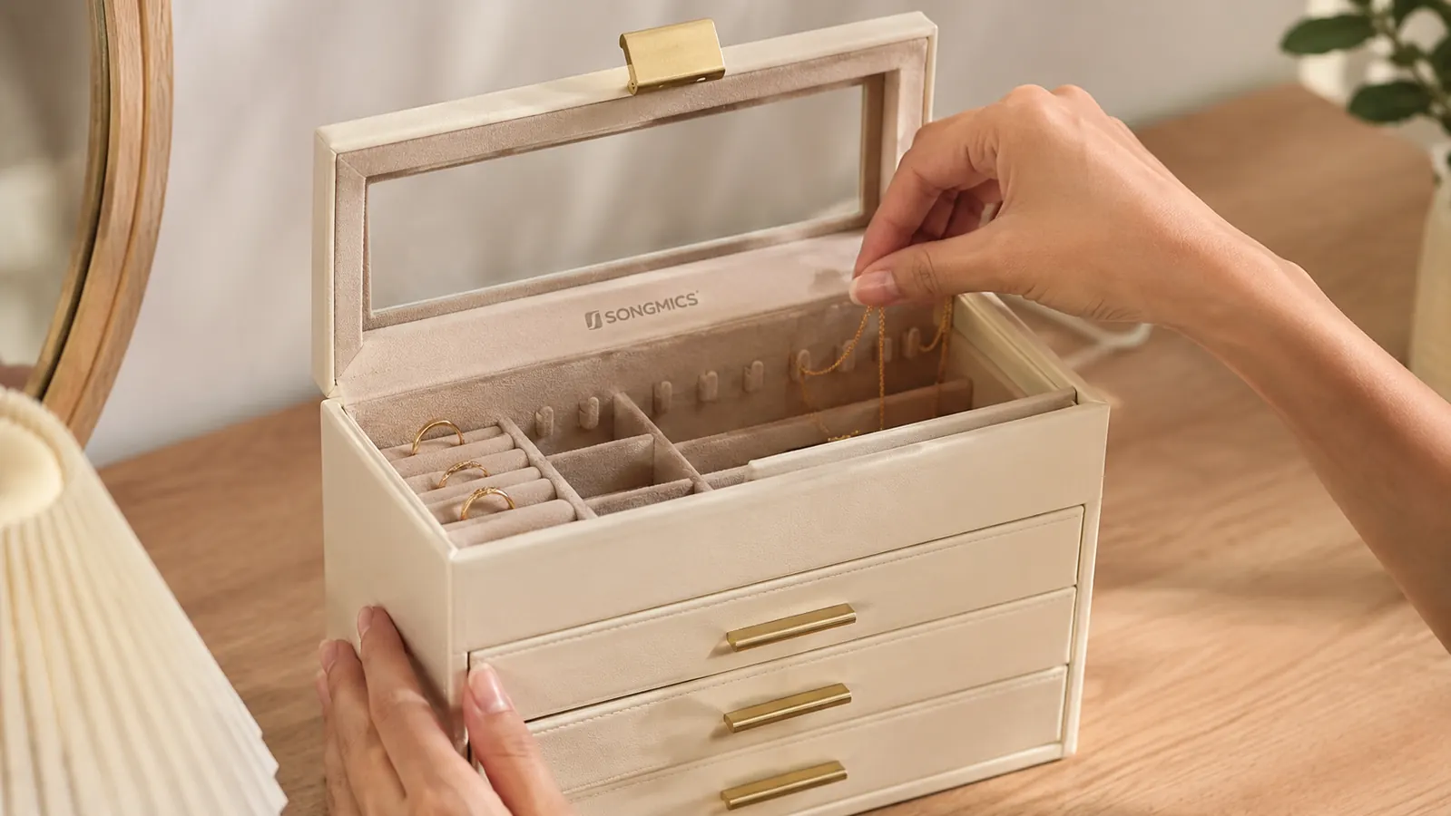 A hand hanging an untangled necklace on one of the interior hooks inside the SONGMICS glass-lid jewelry box