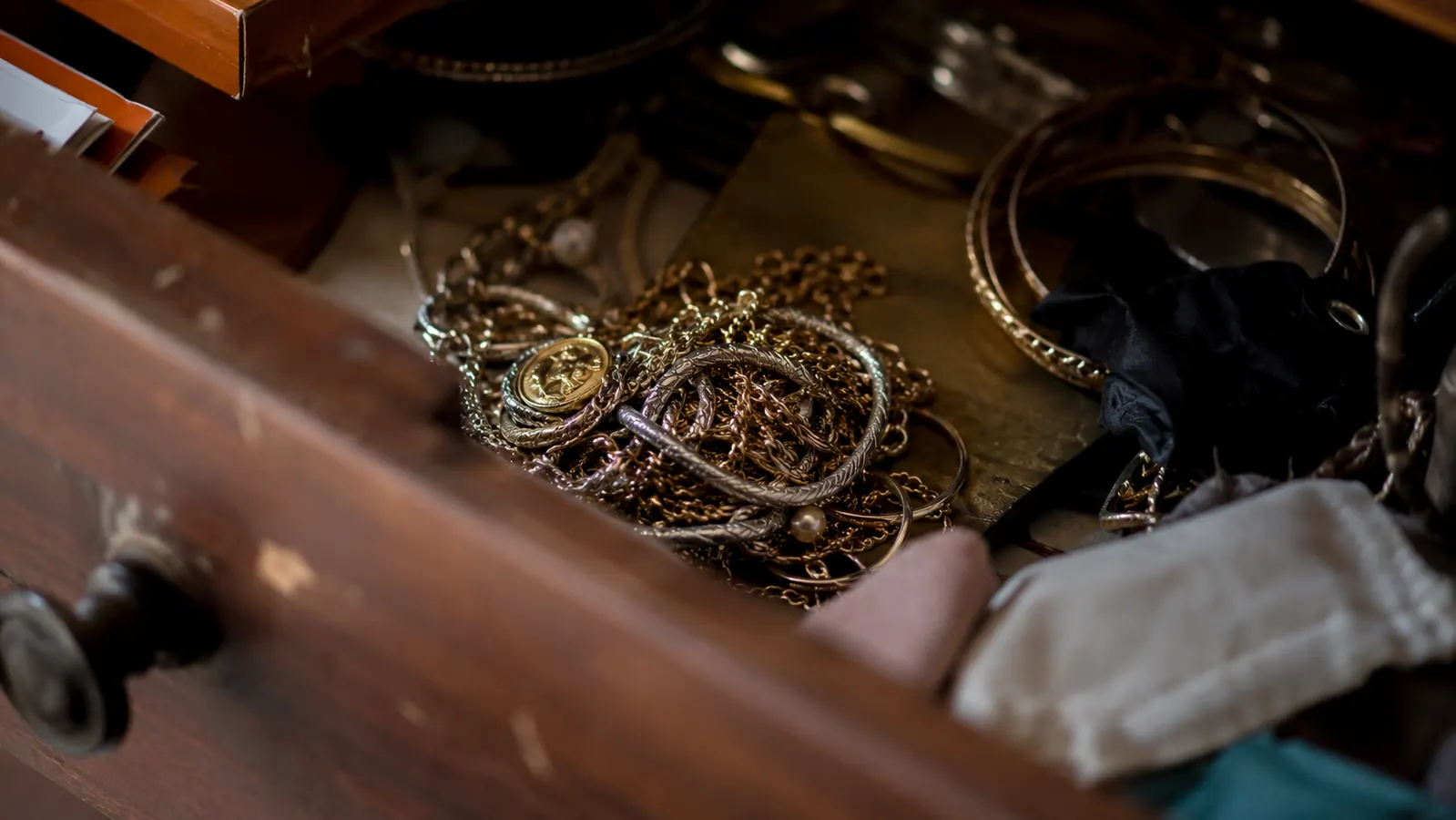 A tangled ball of necklaces and chains spilling out of an open dresser drawer