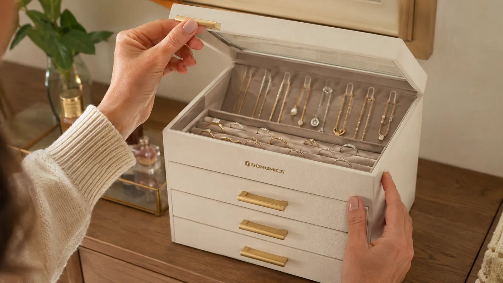 Hand lifting the glass lid of the SONGMICS jewelry box to reveal necklace hooks and ring rolls inside